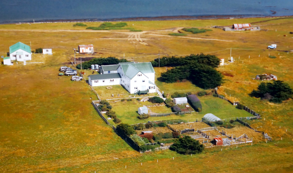 Luftaufnahme der Pebble Lodge, umgeben von grünen Wiesen und nahe einem Küstengewässer